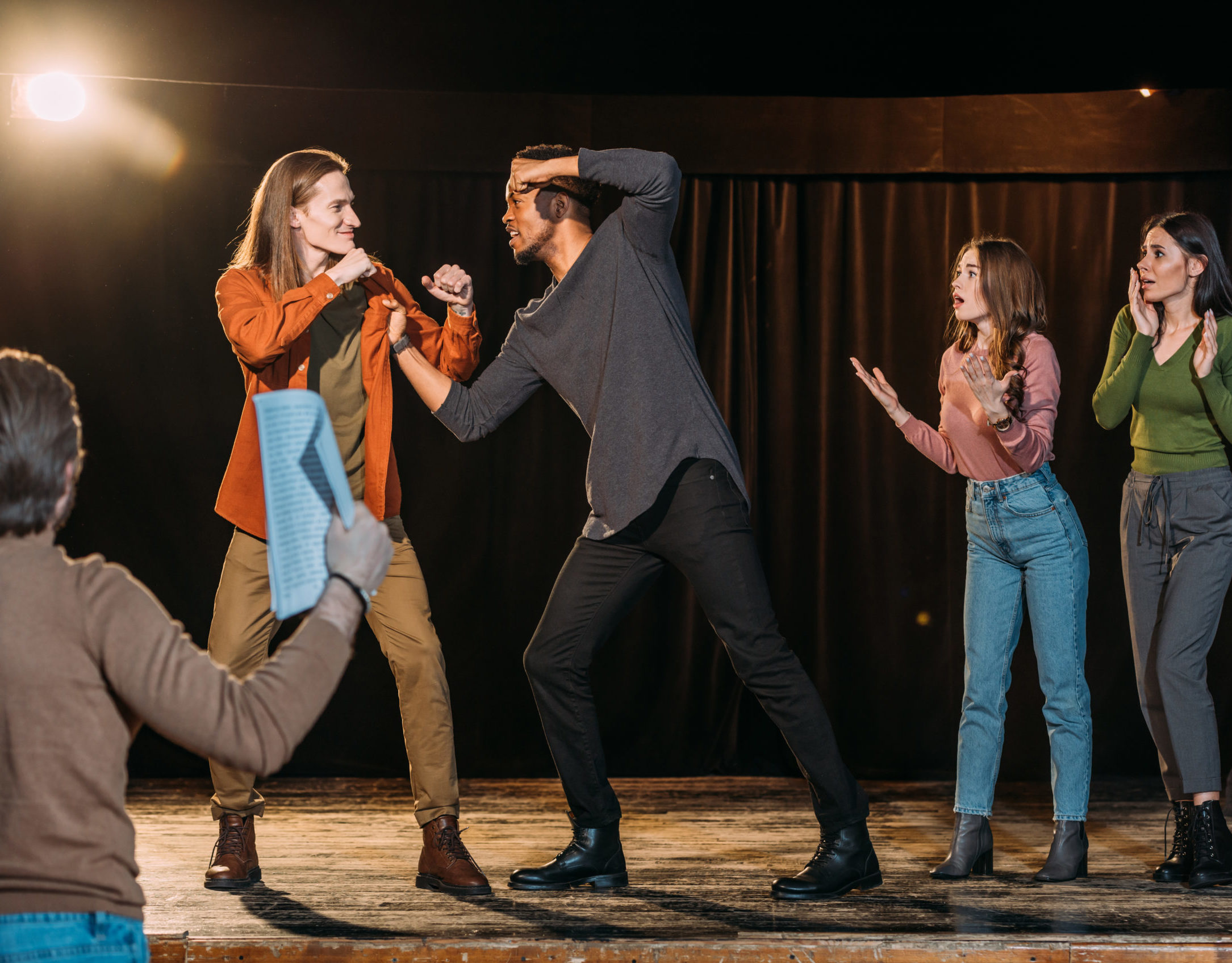 multicultural actors rehearsing fight on stage in theatre